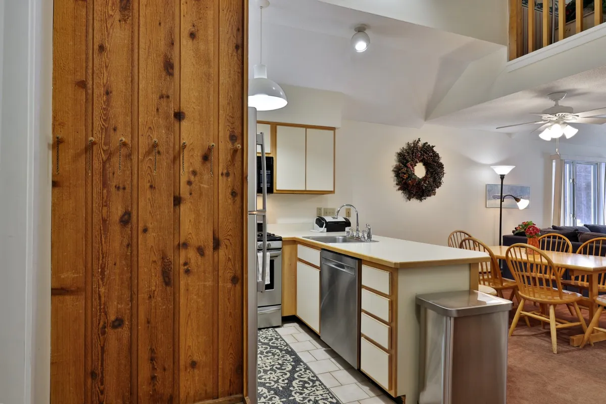 A modern, fully equipped kitchen with a central island, stainless steel appliances, and wooden cabinetry. The kitchen opens towards a dining table, illustrating a seamless flow between cooking and dining spaces ideal for shared meals and celebrations.