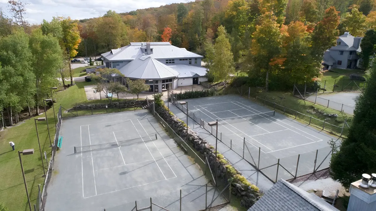 Outdoor tennis courts surrounded by trees and the main building, with vibrant activity and scenic views—inviting residents to enjoy friendly matches and seasonal outdoor recreation.