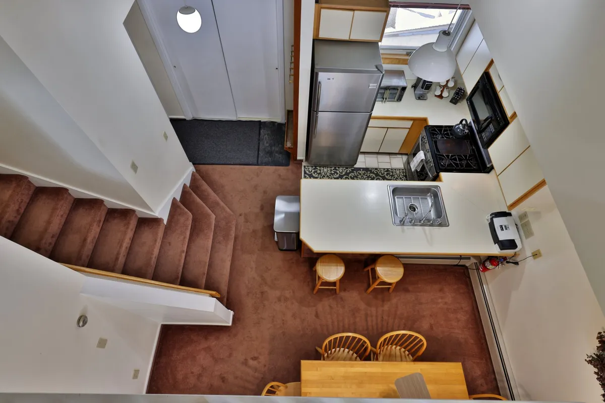 An open-plan kitchen and dining area with a central island, staircase, and table, set in a cozy, home-like environment. The scene suggests possibilities for shared meals, celebrations, and casual gatherings.