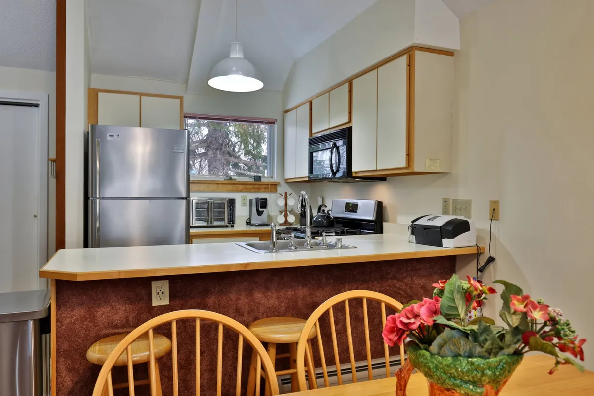 A bright, modern kitchen with a central island, sleek stainless steel appliances, and a vibrant flower arrangement. The space looks inviting for meal preparation and post-adventure family gatherings.