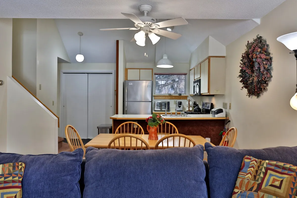 A bright, open space featuring a dining table adjacent to the kitchen area and a comfortable sofa. Large windows and a decorative wreath add to the inviting, festive atmosphere, with natural light filling the room.