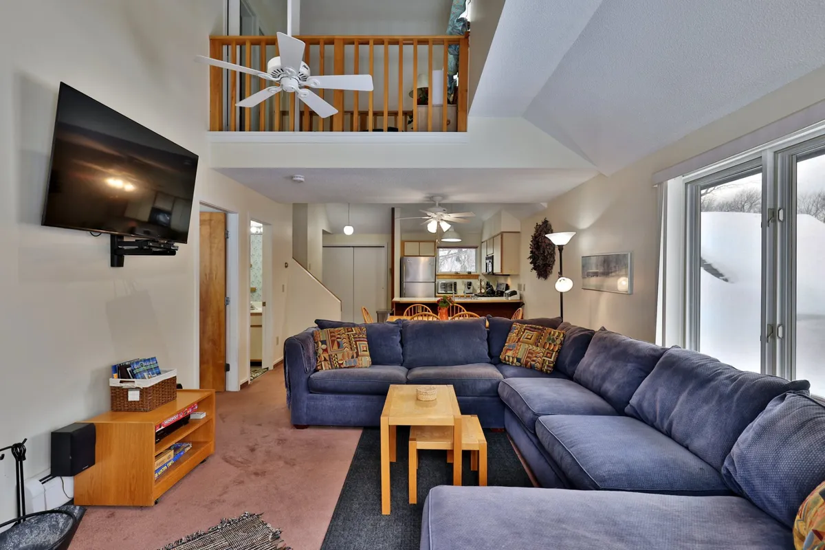 A large sectional sofa arranged around a wooden coffee table with a TV mounted on the wall, and a window offering a view of snow outside. The space is cozy, ideal for movie nights, games, or simply relaxing together.
