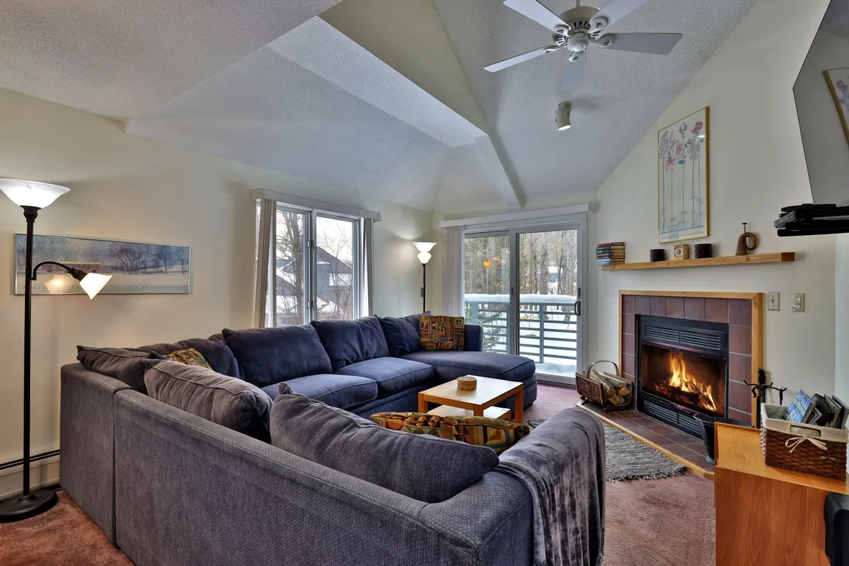 A large sectional sofa faces a cozy fireplace and coffee table, with windows framing serene outdoor views. The room exudes comfort, with plush seating and warm lighting inviting relaxation or socializing after a day of adventure.