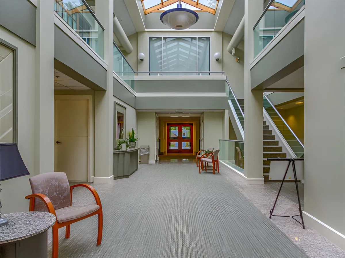 A welcoming reception area bathed in natural light from a large skylight, featuring a staircase and comfortable seating. The space has an inviting, open feel, suggesting an easy arrival experience and a pleasant transition from outdoors to indoors.