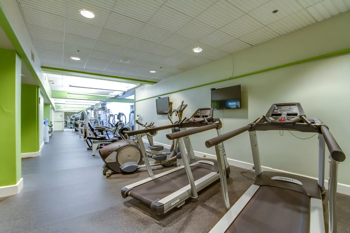 A modern fitness center equipped with treadmills, elliptical machines, exercise bikes, and television screens, offering a motivating and energetic environment for workouts and group classes.