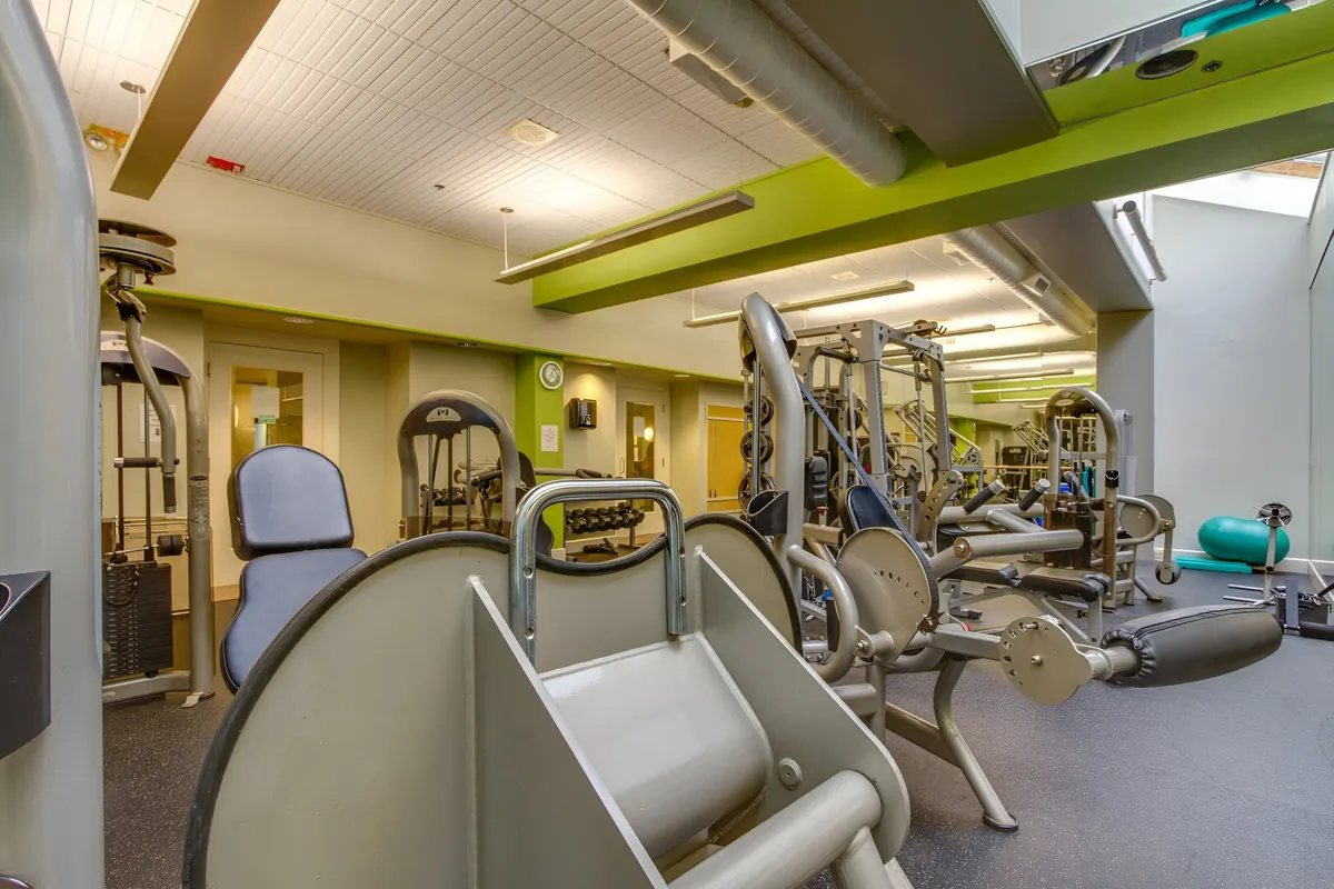 This image showcases a modern gym with exercise machines, a weight lifting area, and stretching mats. The setup highlights a motivational environment for working out, group fitness classes, or personal training sessions.