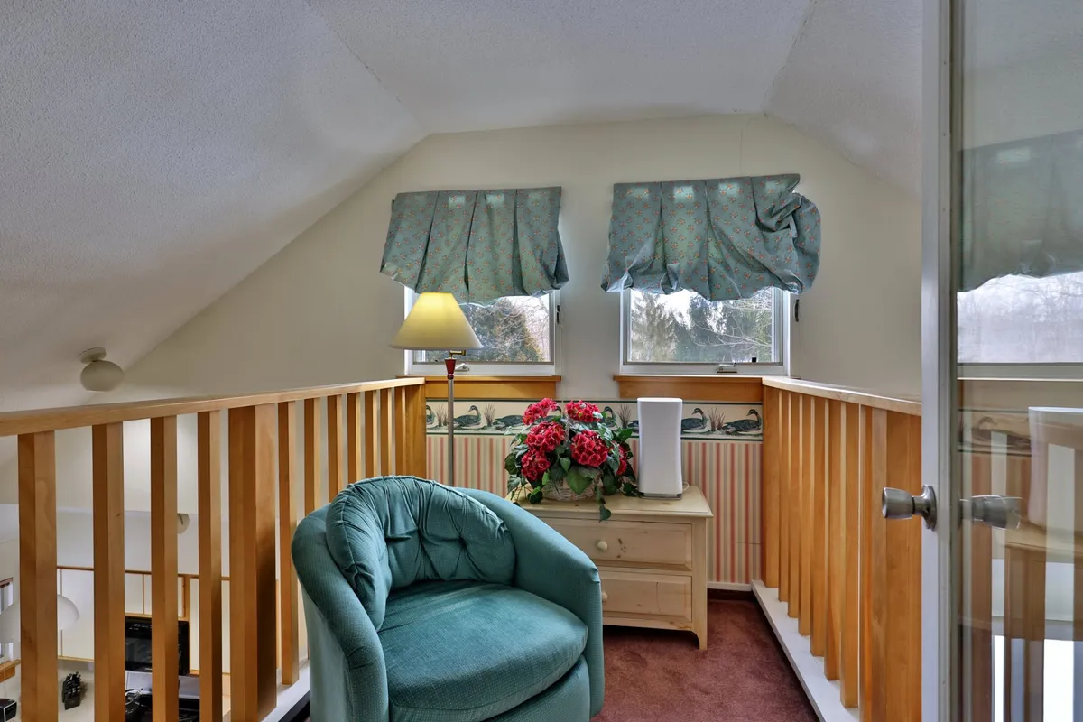 A cozy corner with an armchair, elegant lamp, flower arrangement, and window treatments. The window lets in light and hints at relaxing with views of the outdoors.