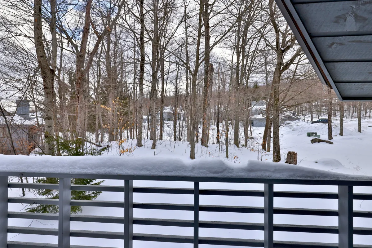 A peaceful exterior view featuring snow-covered trees, distant homes, and a deck railing. The scene invites quiet reflection, relaxation, and an appreciation of Killington’s winter wonderland.