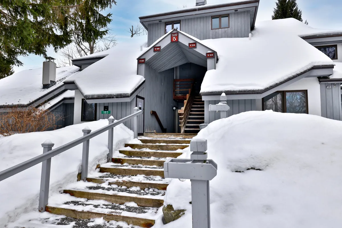 A close-up of the welcoming building entrance, with snow-covered steps, a wooden railing, and a numbered door. The scene radiates a cozy ambiance and suggests a warm retreat after a day outdoors.