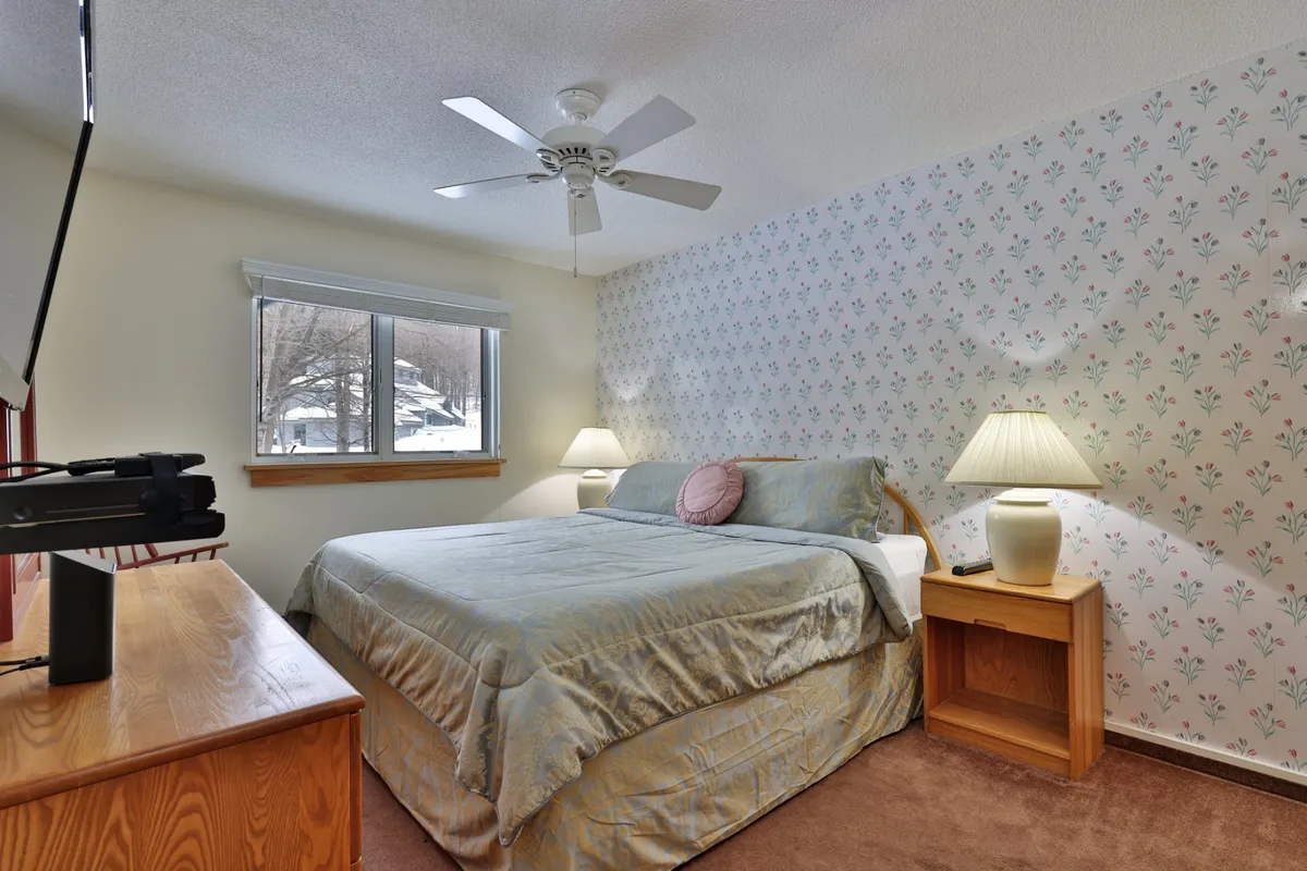 A cozy bedroom featuring a comfortable bed, bedside lamps, window with a serene view, and patterned wallpaper. The soft lighting and inviting decor provide an ideal spot for relaxation and quiet moments.