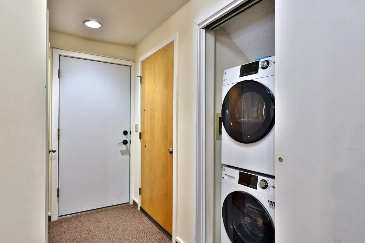 This image captures the entry area, featuring a sturdy front door, hallway lighting, and laundry appliances. The scene conveys a sense of organization, warmth, and everyday functionality—key to the feeling of comfort and security.