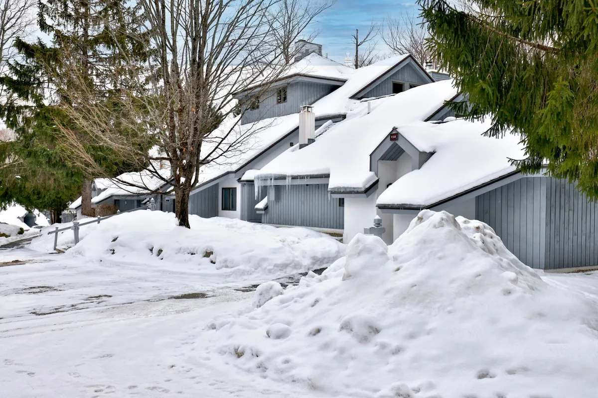 A serene winter exterior scene showcasing snow-covered rooftops and tree branches, with ample piles of fresh snow enveloping the area. The peaceful landscape hints at both the excitement of winter sports and the cozy relaxation that follows outdoor adventures.